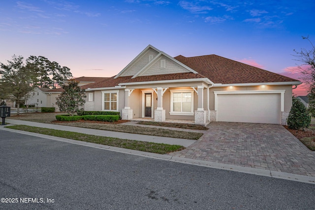 craftsman inspired home with decorative driveway, a garage, a shingled roof, and stucco siding