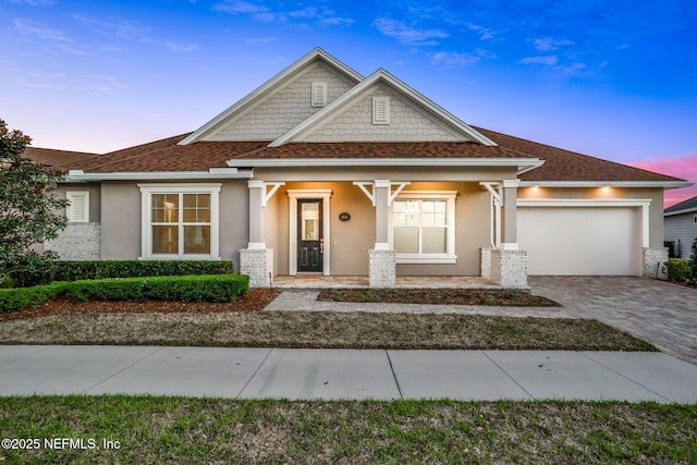 craftsman-style home with stucco siding, decorative driveway, a garage, and roof with shingles