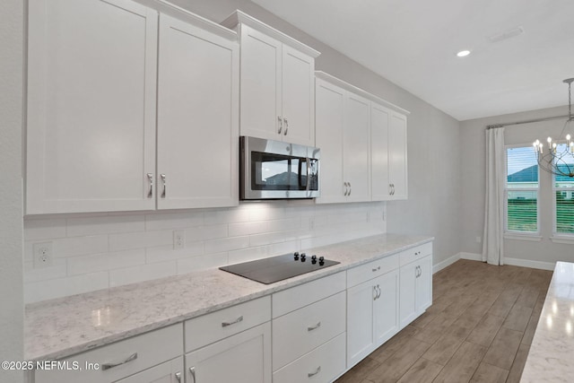 kitchen featuring stainless steel microwave, black electric stovetop, white cabinets, and decorative backsplash