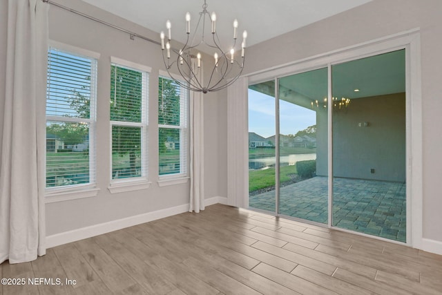 empty room with a notable chandelier, wood finished floors, and baseboards