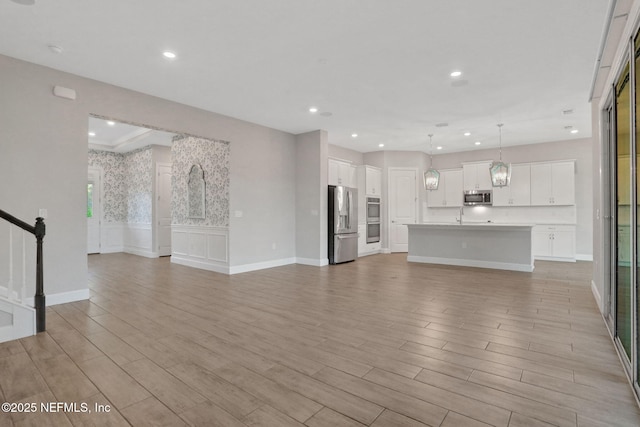 unfurnished living room featuring a wainscoted wall, recessed lighting, stairs, and light wood-style floors