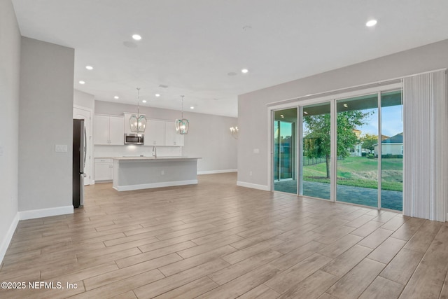 unfurnished living room with recessed lighting, baseboards, a chandelier, and light wood finished floors