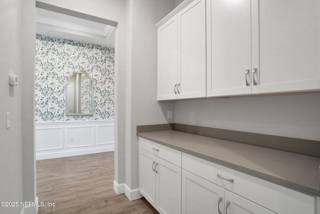 bar featuring light wood-type flooring, a decorative wall, wainscoting, and crown molding