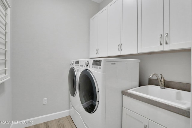 clothes washing area with baseboards, light wood-style flooring, cabinet space, a sink, and washing machine and dryer