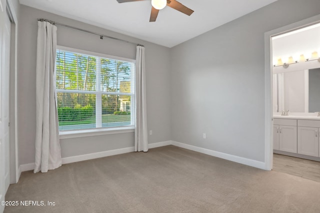 unfurnished bedroom with light colored carpet, ensuite bathroom, baseboards, and ceiling fan