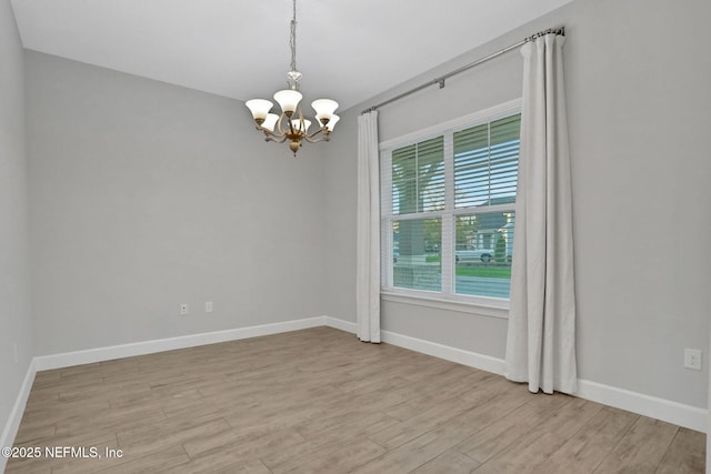 unfurnished room with an inviting chandelier, light wood-style floors, and baseboards