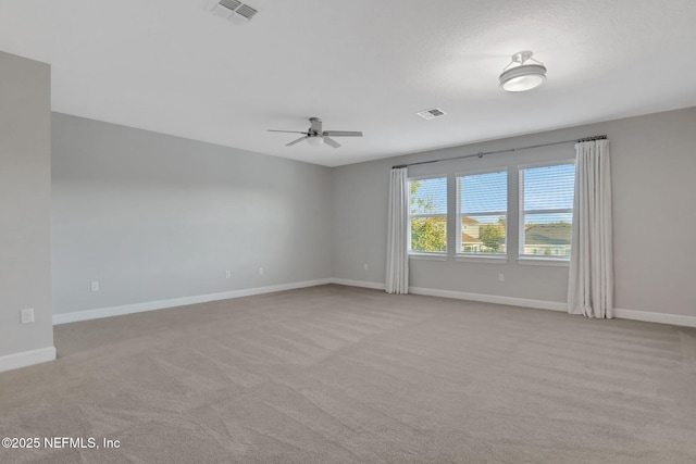 spare room with light colored carpet, baseboards, visible vents, and ceiling fan