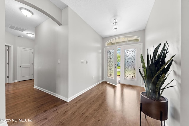 foyer with visible vents, a textured ceiling, wood finished floors, arched walkways, and baseboards