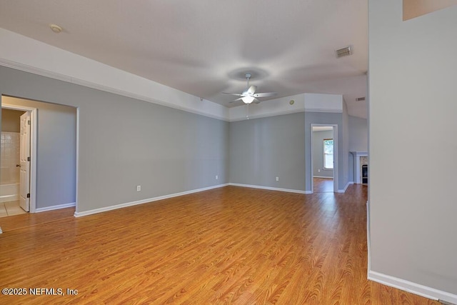 spare room featuring light wood finished floors, visible vents, baseboards, a tile fireplace, and a ceiling fan