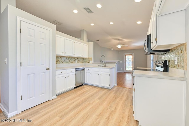 kitchen featuring visible vents, a peninsula, a sink, stainless steel appliances, and white cabinets