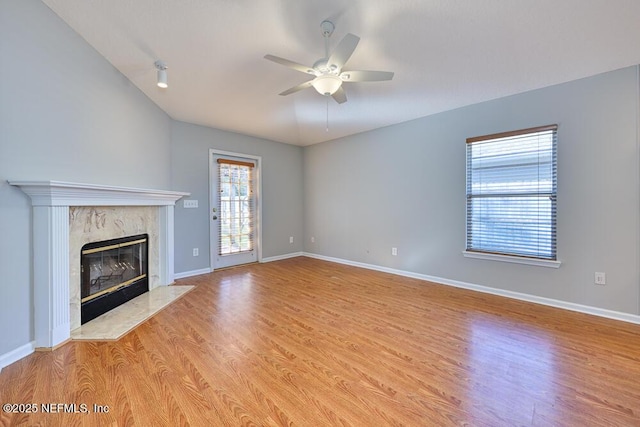 unfurnished living room featuring ceiling fan, a fireplace, baseboards, and light wood-style floors