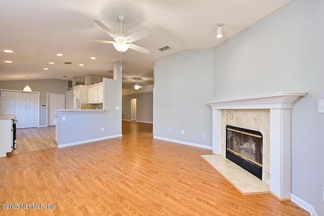 unfurnished living room with visible vents, baseboards, a premium fireplace, vaulted ceiling, and light wood-style floors