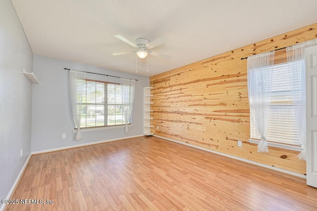 spare room with wood walls, baseboards, ceiling fan, and wood finished floors