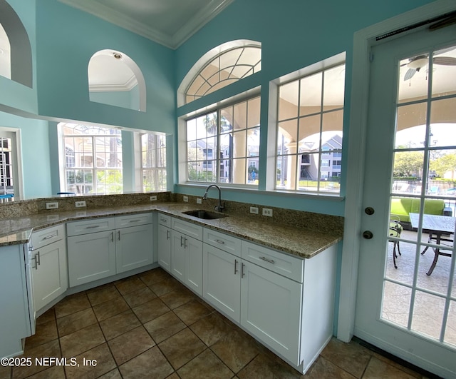 kitchen featuring a healthy amount of sunlight, dark tile patterned flooring, ornamental molding, a sink, and white cabinetry