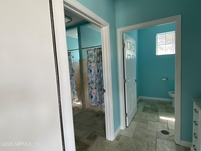 full bathroom with vanity, a shower with curtain, baseboards, stone finish floor, and toilet