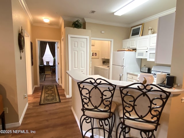 kitchen with ornamental molding, washer and dryer, wood finished floors, white cabinetry, and white appliances