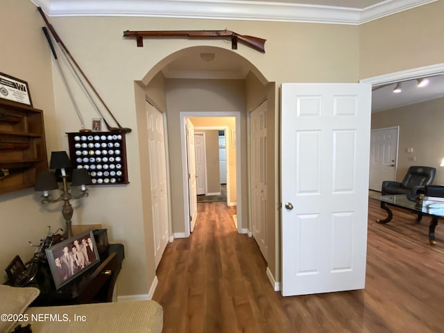 hallway featuring baseboards, wood finished floors, arched walkways, and ornamental molding