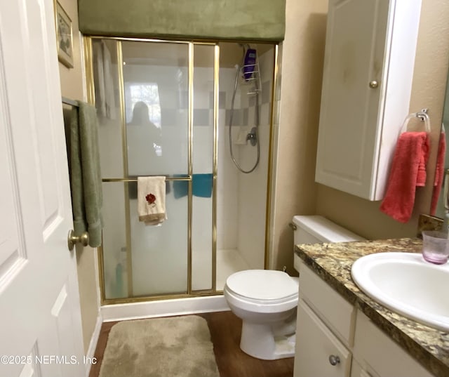 bathroom with vanity, toilet, wood finished floors, and a stall shower