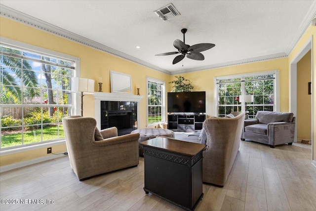 living area featuring visible vents, ornamental molding, a fireplace, and light wood-style flooring