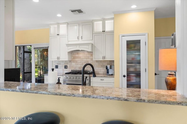 kitchen with decorative backsplash, light stone countertops, visible vents, and high end stainless steel range