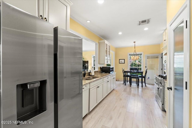 kitchen with visible vents, light stone countertops, light wood-type flooring, stainless steel appliances, and a sink