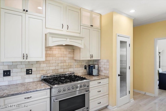 kitchen with tasteful backsplash, glass insert cabinets, custom range hood, light stone counters, and high end stainless steel range oven