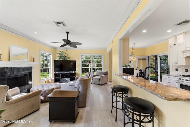 living area featuring visible vents, ceiling fan, ornamental molding, a tiled fireplace, and light wood-type flooring