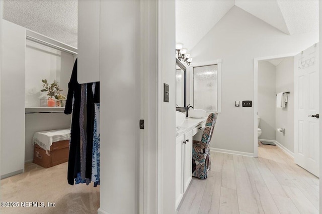 bathroom featuring wood finished floors, baseboards, lofted ceiling, a textured ceiling, and toilet