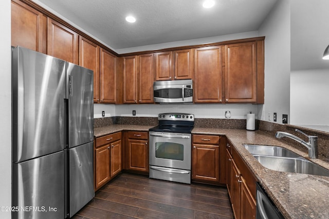 kitchen with a sink, dark stone countertops, dark wood finished floors, stainless steel appliances, and brown cabinetry