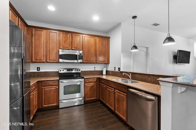 kitchen with dark wood finished floors, a peninsula, a sink, stainless steel appliances, and brown cabinets