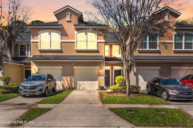 view of property featuring stucco siding, an attached garage, driveway, and roof with shingles