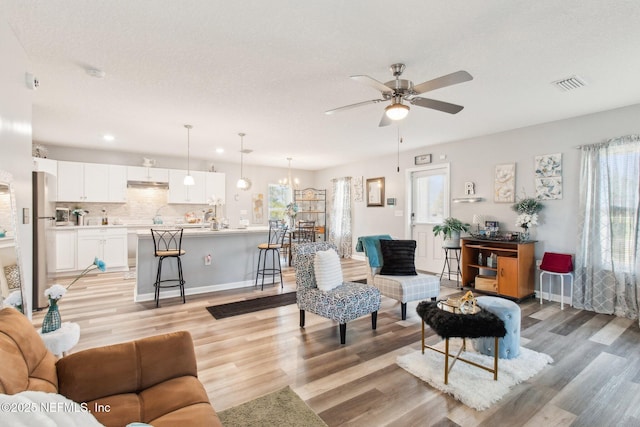 living room featuring visible vents, a ceiling fan, a textured ceiling, light wood-style floors, and baseboards