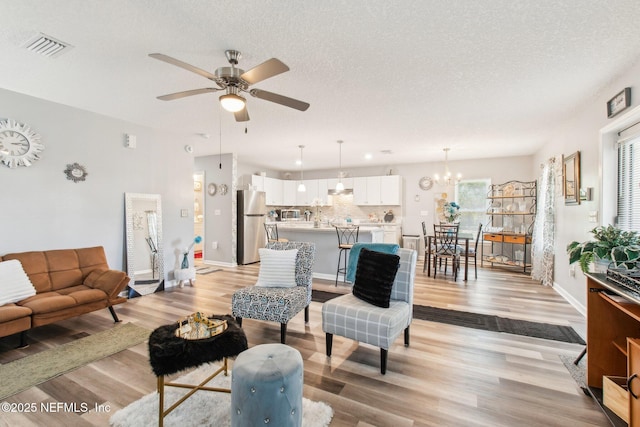 living area with light wood finished floors, visible vents, ceiling fan with notable chandelier, and a textured ceiling