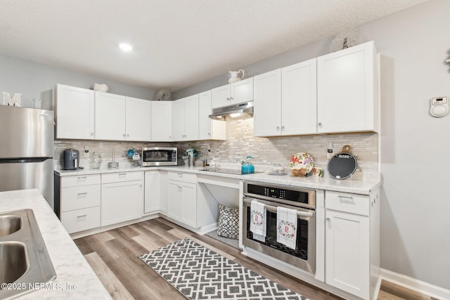 kitchen with a sink, stainless steel appliances, light countertops, light wood-style floors, and under cabinet range hood