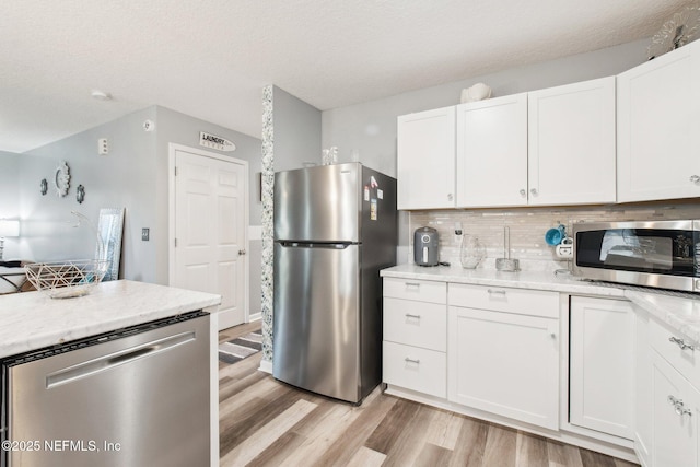 kitchen with light wood-type flooring, decorative backsplash, appliances with stainless steel finishes, a textured ceiling, and white cabinetry