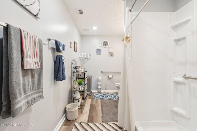 full bathroom featuring visible vents, a stall shower, a textured ceiling, wood finished floors, and baseboards