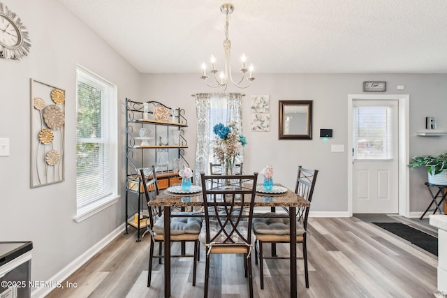 dining space featuring a chandelier, a textured ceiling, baseboards, and light wood-style floors