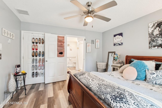 bedroom with visible vents, light wood-type flooring, ensuite bath, a textured ceiling, and a ceiling fan