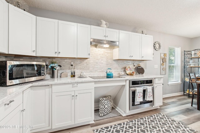 kitchen with under cabinet range hood, backsplash, appliances with stainless steel finishes, white cabinets, and light wood finished floors