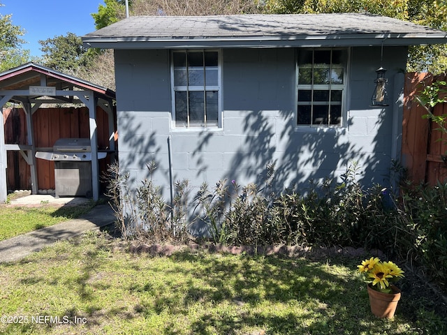 view of side of home with a shingled roof, a lawn, concrete block siding, and fence