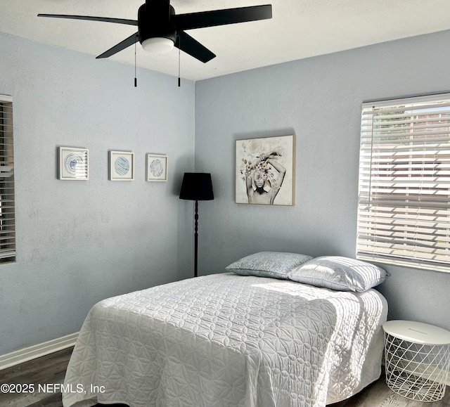 bedroom featuring ceiling fan, baseboards, wood finished floors, and a textured wall