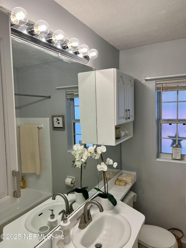 bathroom featuring a sink, a textured ceiling, a bath, and toilet