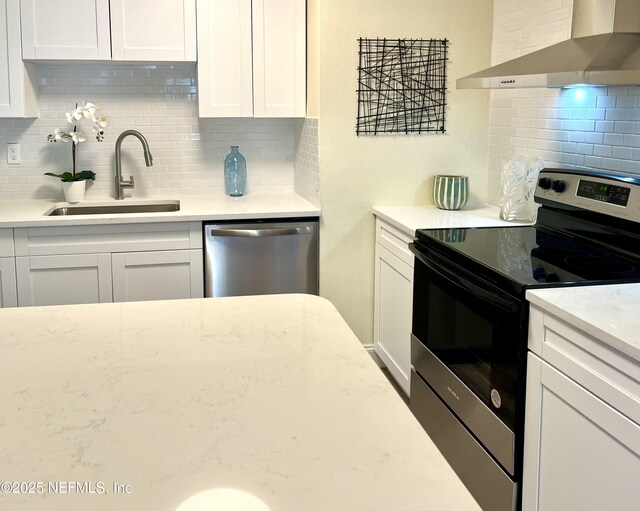 kitchen featuring a sink, white cabinetry, stainless steel appliances, wall chimney exhaust hood, and decorative backsplash