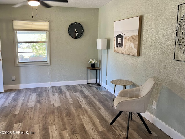 sitting room featuring baseboards, wood finished floors, a ceiling fan, and a textured wall