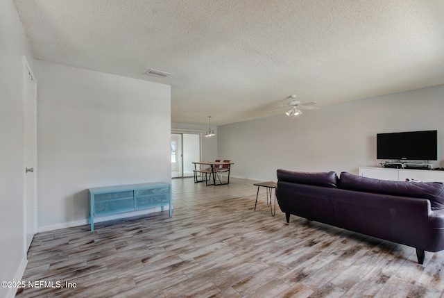 living room featuring wood finished floors, baseboards, visible vents, ceiling fan, and a textured ceiling