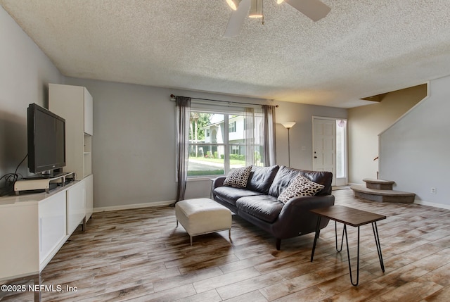 living room with baseboards, a textured ceiling, a ceiling fan, and light wood finished floors