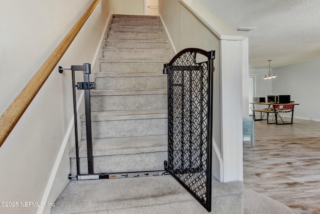 staircase featuring wood finished floors, baseboards, visible vents, an inviting chandelier, and a textured ceiling