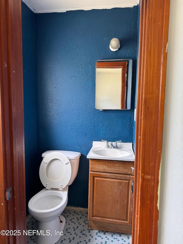 half bathroom featuring vanity, toilet, and a textured wall