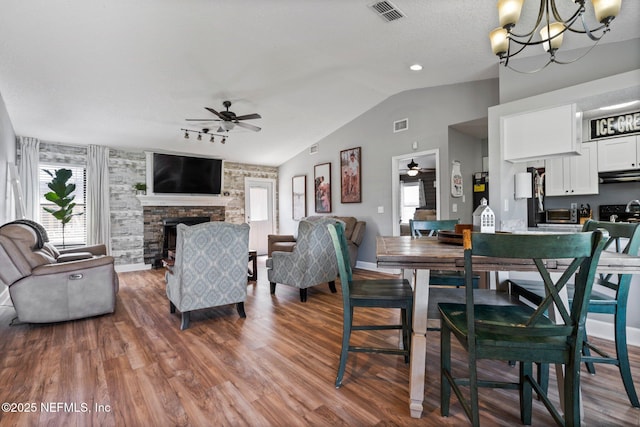 dining area with visible vents, lofted ceiling, ceiling fan with notable chandelier, a fireplace, and wood finished floors