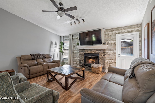 living area featuring track lighting, a ceiling fan, a textured ceiling, wood finished floors, and a large fireplace